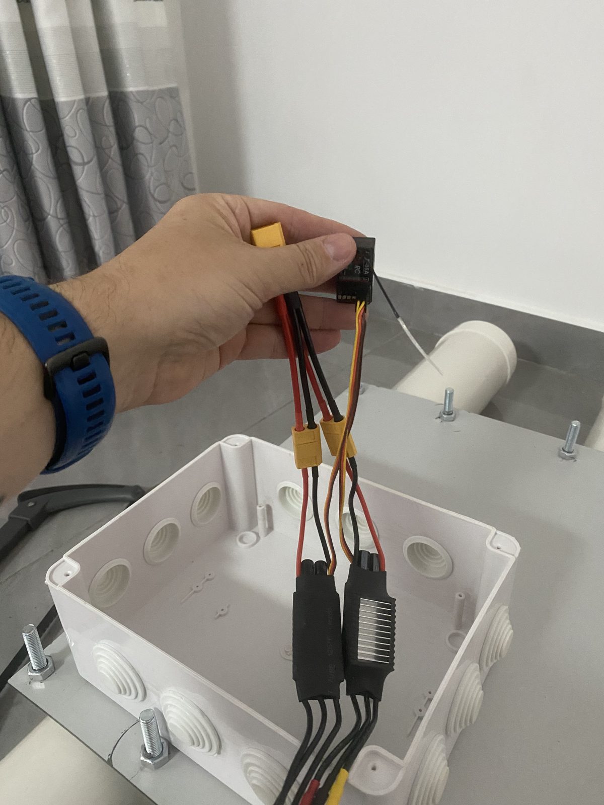 Hand holding the twin ESC and XT60 power harness above the open junction box